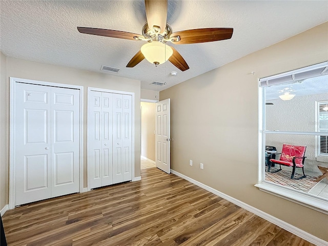 bedroom with a textured ceiling, two closets, dark wood-type flooring, and ceiling fan