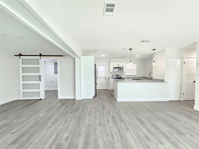 kitchen with kitchen peninsula, light hardwood / wood-style flooring, a barn door, decorative light fixtures, and white cabinetry