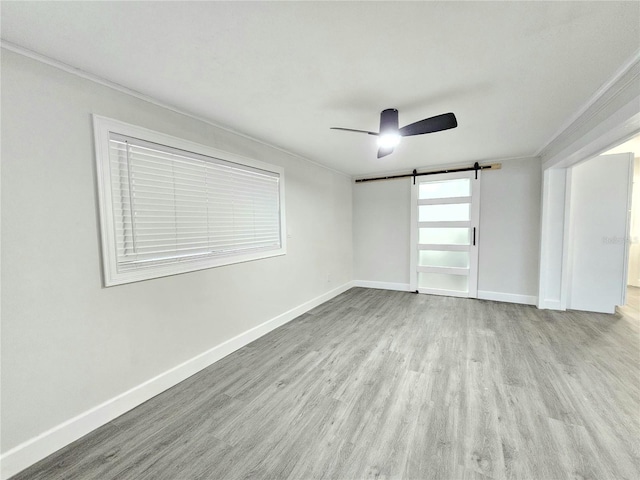 unfurnished room with ceiling fan, a barn door, ornamental molding, and light hardwood / wood-style flooring