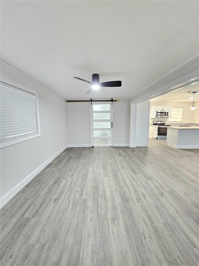 unfurnished living room featuring a barn door, light hardwood / wood-style floors, ceiling fan, and ornamental molding