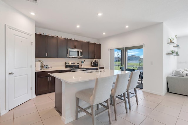 kitchen with appliances with stainless steel finishes, sink, an island with sink, dark brown cabinetry, and light tile patterned floors