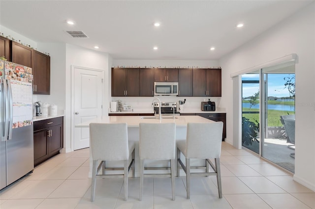 kitchen with a kitchen island with sink, dark brown cabinets, appliances with stainless steel finishes, and a water view