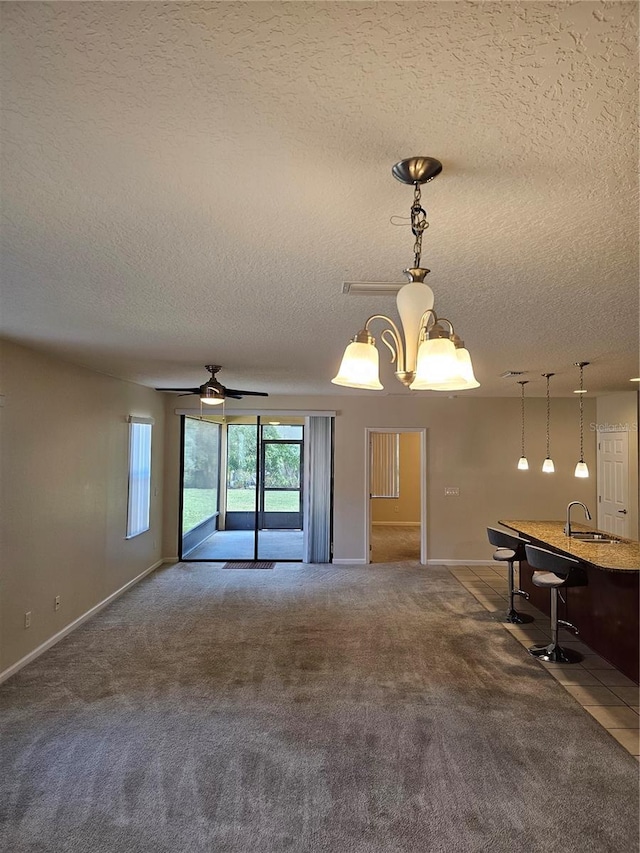 unfurnished living room with carpet, a textured ceiling, ceiling fan with notable chandelier, and sink