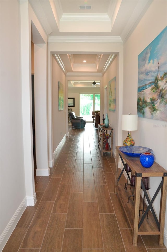 corridor with ornamental molding, dark hardwood / wood-style floors, and a raised ceiling