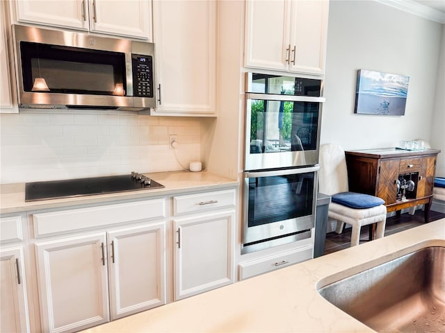 kitchen with appliances with stainless steel finishes, backsplash, white cabinets, light stone counters, and ornamental molding