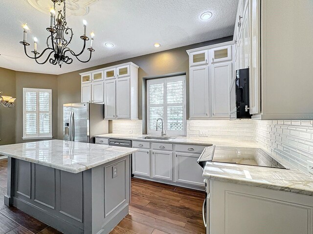 kitchen featuring stainless steel fridge, light stone counters, a kitchen island, white cabinetry, and sink