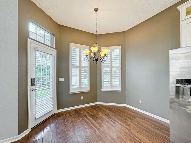 unfurnished dining area with an inviting chandelier, a textured ceiling, and wood-type flooring