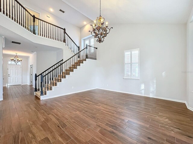 unfurnished living room with a wealth of natural light, dark wood-type flooring, an inviting chandelier, and high vaulted ceiling