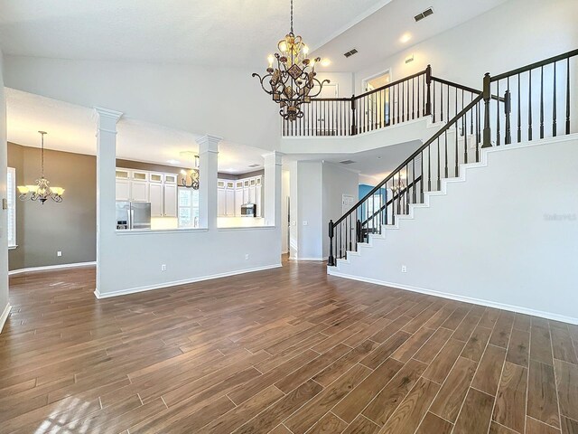 unfurnished living room with dark hardwood / wood-style floors, high vaulted ceiling, and ornate columns