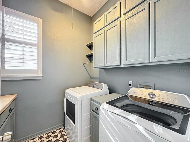 laundry area with a textured ceiling, cabinets, and washing machine and clothes dryer