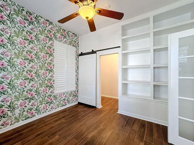 unfurnished bedroom featuring dark hardwood / wood-style flooring, a textured ceiling, a barn door, and ceiling fan