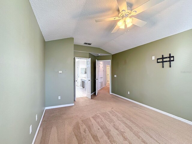 unfurnished bedroom featuring lofted ceiling, ceiling fan, a textured ceiling, ensuite bath, and light colored carpet