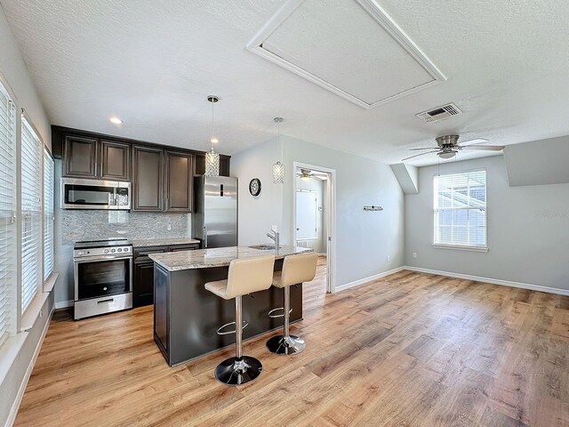 kitchen featuring a breakfast bar area, a center island with sink, light wood-type flooring, appliances with stainless steel finishes, and tasteful backsplash