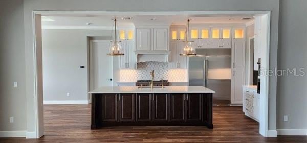 kitchen with a center island with sink, dark wood-type flooring, built in fridge, and pendant lighting