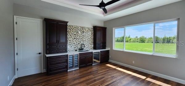 bar with dark wood-type flooring, wine cooler, a tray ceiling, and ceiling fan