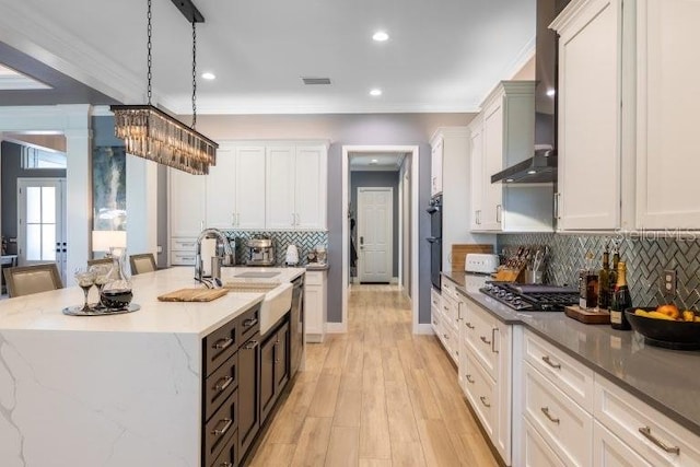 kitchen featuring wall chimney range hood, a center island with sink, hanging light fixtures, backsplash, and a kitchen bar