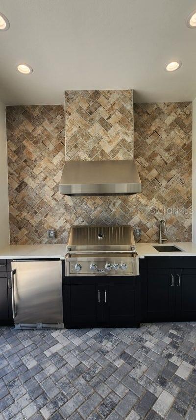 kitchen with wall chimney exhaust hood, sink, tasteful backsplash, and stainless steel refrigerator