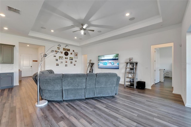 living area featuring crown molding, visible vents, a raised ceiling, and wood finished floors