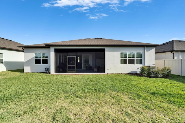 rear view of house with a yard, fence, a sunroom, and stucco siding