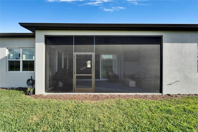 back of house with a lawn, a sunroom, and stucco siding