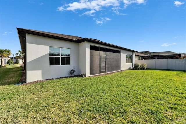 rear view of house with fence, a lawn, and stucco siding