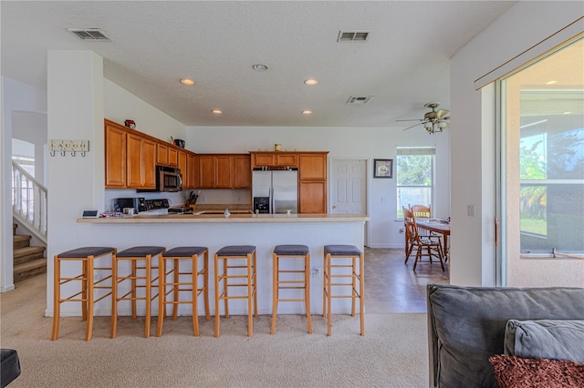 kitchen featuring a textured ceiling, appliances with stainless steel finishes, a breakfast bar area, and kitchen peninsula