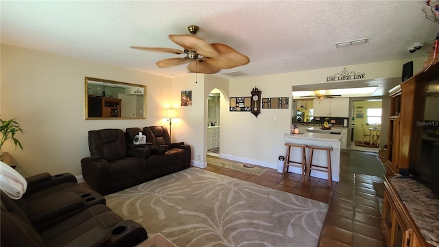 living room with a textured ceiling, dark tile patterned floors, and ceiling fan