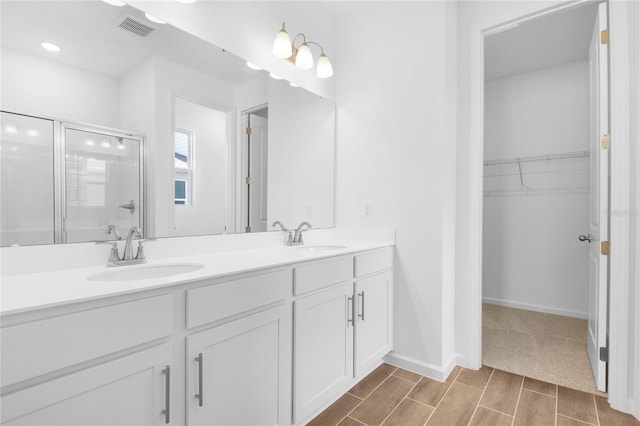 bathroom with a sink, a walk in closet, a stall shower, and visible vents