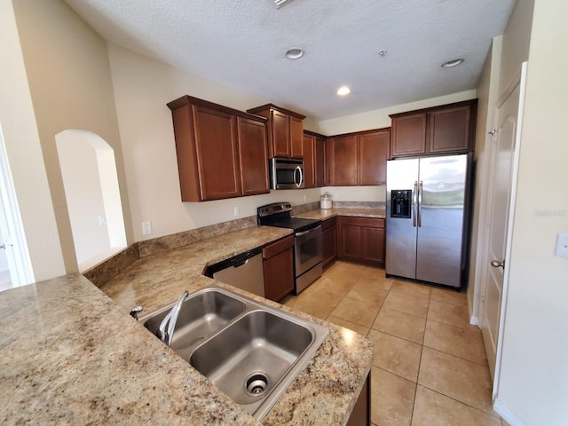 kitchen with sink, kitchen peninsula, stainless steel appliances, light stone counters, and light tile patterned floors