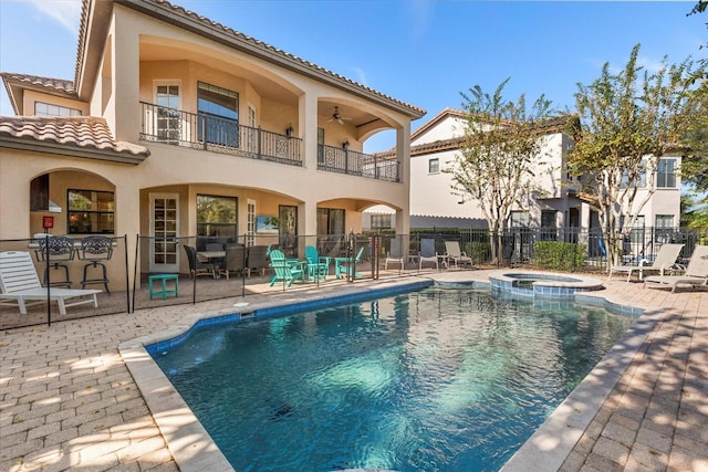 rear view of house with a balcony, a patio, and a pool with hot tub