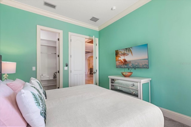 bedroom featuring a closet, crown molding, carpet flooring, and a walk in closet