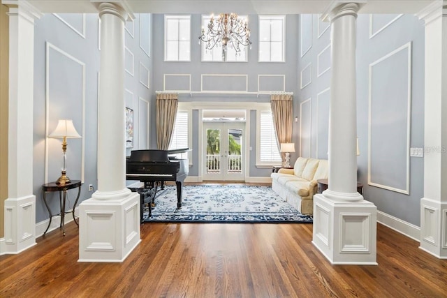 living area with dark wood-type flooring, a notable chandelier, a healthy amount of sunlight, and decorative columns