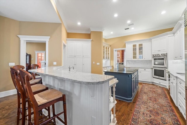 kitchen featuring tasteful backsplash, dark hardwood / wood-style flooring, a kitchen breakfast bar, white cabinets, and a center island with sink