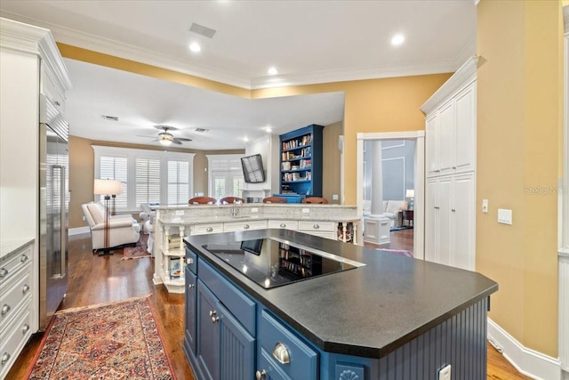 kitchen with black electric stovetop, dark wood-type flooring, a center island, blue cabinetry, and white cabinetry