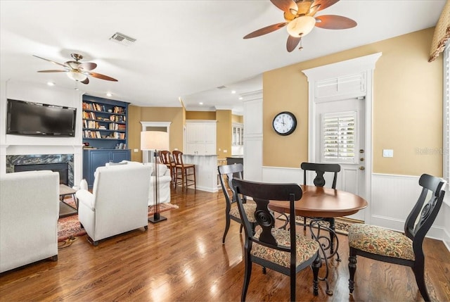 dining space featuring a high end fireplace, built in shelves, wood-type flooring, and ceiling fan