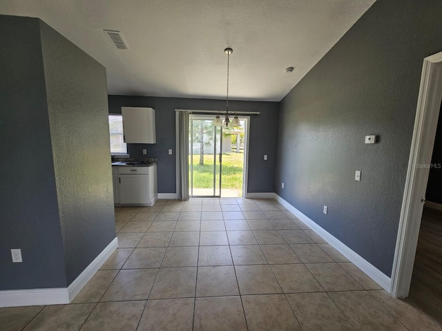 unfurnished dining area featuring an inviting chandelier, vaulted ceiling, and light tile patterned floors