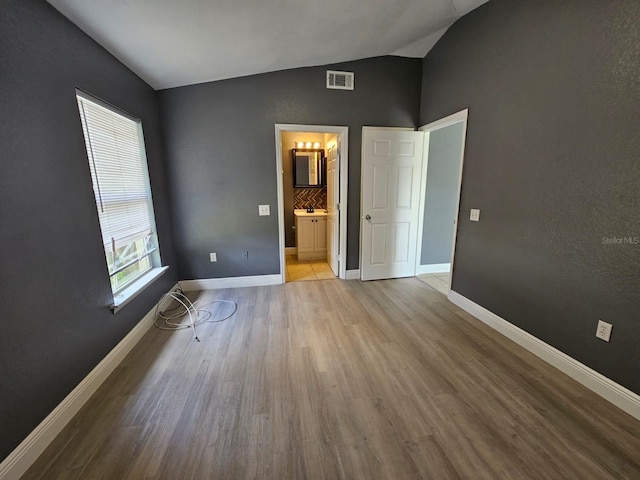 unfurnished bedroom with connected bathroom, vaulted ceiling, and light wood-type flooring