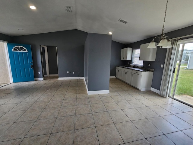 kitchen featuring white cabinets, vaulted ceiling, light tile patterned flooring, pendant lighting, and a notable chandelier