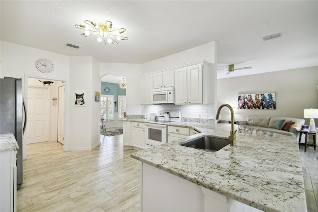 kitchen featuring kitchen peninsula, light stone counters, white appliances, sink, and white cabinets