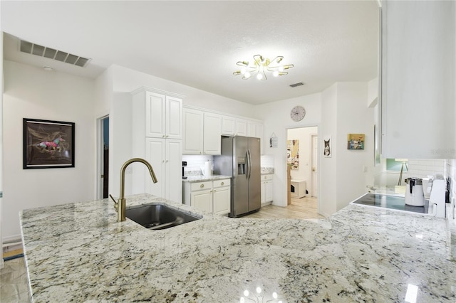 kitchen featuring light stone countertops, stainless steel refrigerator with ice dispenser, white cabinetry, and sink