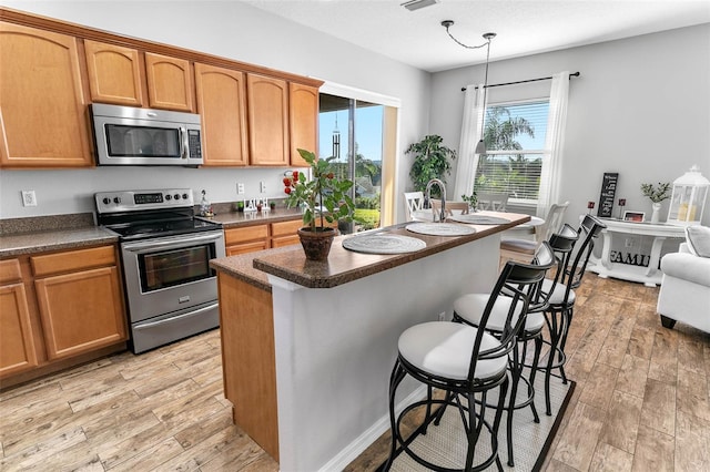 12213 Still Meadow Dr, Clermont, FL 34711 - kitchen featuring stainless steel appliances, light wood-style floors, a breakfast bar, a center island, and dark countertops
