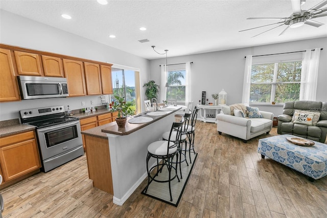12213 Still Meadow Dr, Clermont, FL 34711 - kitchen featuring stainless steel appliances, open floor plan, light wood-style floors, a kitchen bar, and recessed lighting
