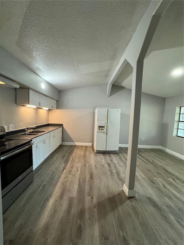 kitchen featuring light wood-type flooring, a textured ceiling, white refrigerator with ice dispenser, white cabinetry, and stainless steel stove