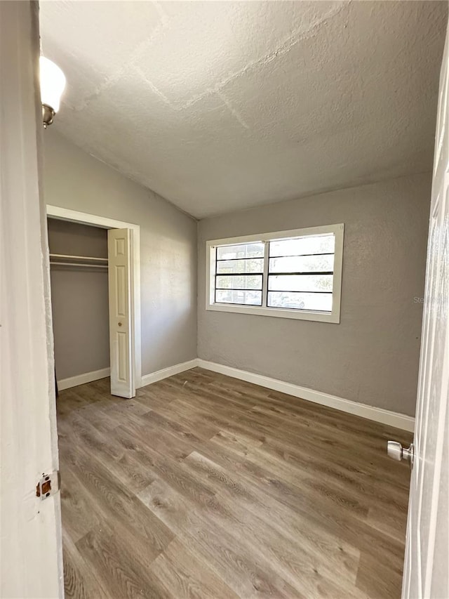 unfurnished bedroom with a closet, hardwood / wood-style flooring, a textured ceiling, and lofted ceiling