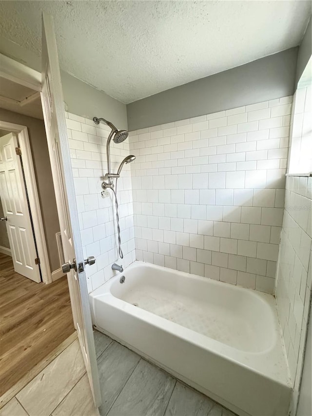 bathroom with tiled shower / bath combo, wood-type flooring, and a textured ceiling