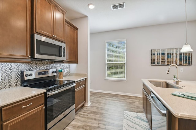 kitchen with light hardwood / wood-style flooring, hanging light fixtures, sink, tasteful backsplash, and appliances with stainless steel finishes