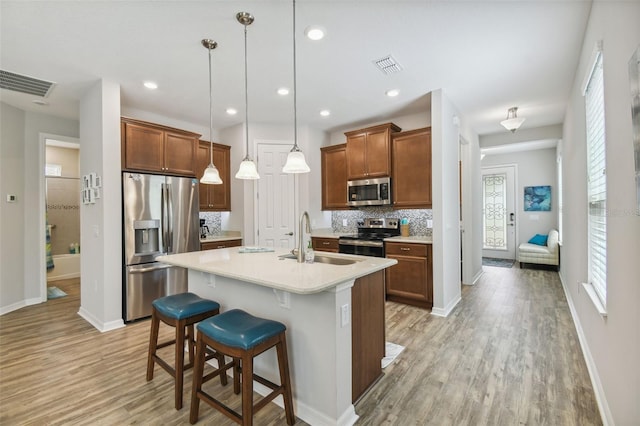 kitchen featuring appliances with stainless steel finishes, decorative light fixtures, a kitchen bar, sink, and a kitchen island with sink