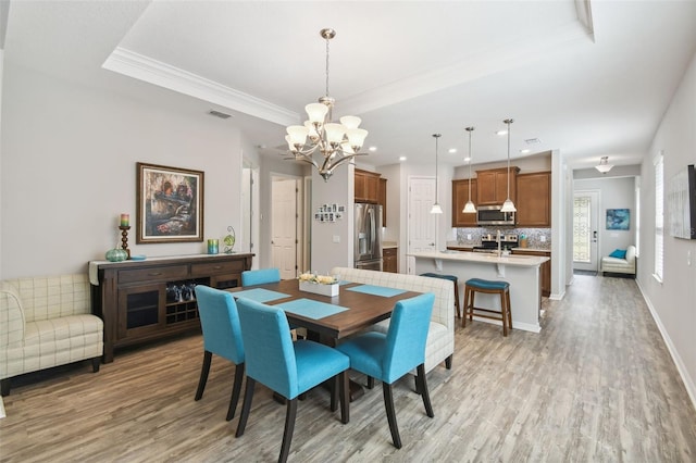 dining room featuring light hardwood / wood-style floors, an inviting chandelier, crown molding, and a tray ceiling