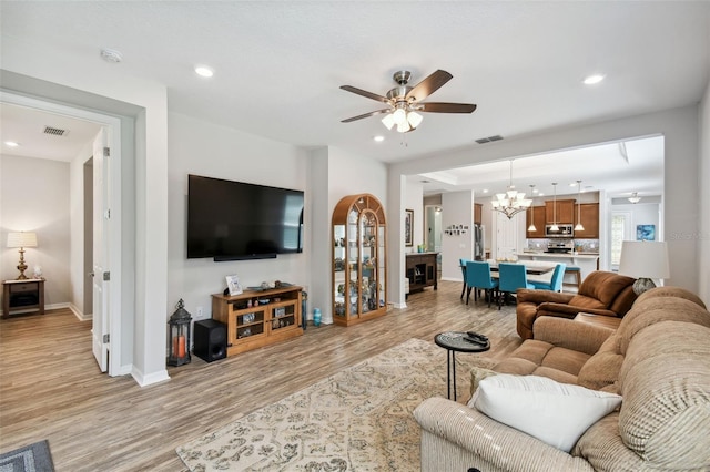 living room with ceiling fan with notable chandelier and light hardwood / wood-style flooring