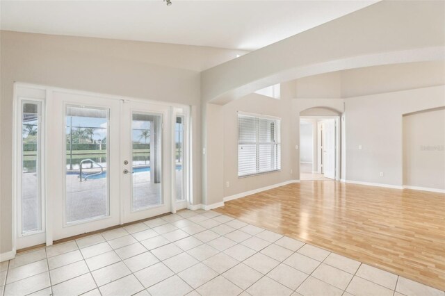 spare room featuring french doors, light hardwood / wood-style flooring, a wealth of natural light, and lofted ceiling